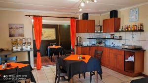 a kitchen with two tables and a kitchen with orange curtains at Premiere Guesthouse in Bloemfontein