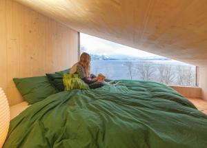 a woman sitting on a bed reading a book at Funkis-cabin in Herand with fantastic fjordview in Samlanes
