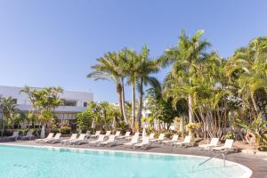 una piscina en el complejo con tumbonas y palmeras en R2 Bahia Playa - Adults Only, en Tarajalejo