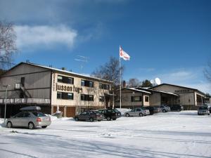 a building with cars parked in a parking lot with a flag at Hotelli Jussan Tupa in Enontekiö