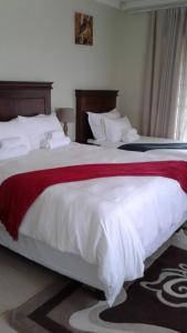 Vinolux Guest House في امتاتا: غرفة نوم بسريرين مع شراشف بيضاء وبطانية حمراء