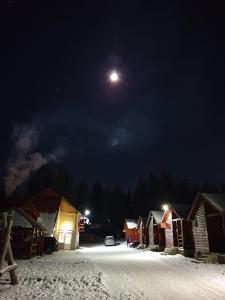 une pleine lune dans le ciel au-dessus d'un village enneigé dans l'établissement Popas Turistic Padis, à Padis