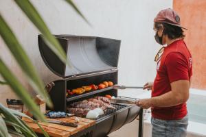 un homme cuisine de la viande et des légumes sur un grill dans l'établissement Hostal Barrio Vivo, à Mérida