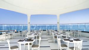 a restaurant with white tables and chairs and windows at INFINITY BY YELKEN AQUAPARK&RESORTS KUŞADASI in Kusadası