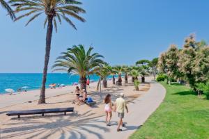 a group of people walking along a beach with palm trees at Apartments Sorrabona in Pineda de Mar