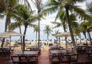 un gruppo di tavoli e sedie su una spiaggia con palme di Apartamento Praia Grande- SP Vila Tupi a Praia Grande