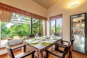 a dining room with a table and chairs and a large window at StayVista's Green Grove - A Modern Mountain-View Retreat with Lush Lawn in Trimbak +17 photos