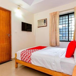 Schlafzimmer mit einem Bett mit roten Kissen und einem Fenster in der Unterkunft TRI-STAR RESIDENCY Cochin in Ernakulam