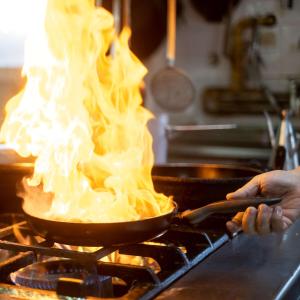 eine Person, die Essen in einer Pfanne mit Flammen kocht in der Unterkunft Best Western Hotel Mediterraneo in Castelldefels