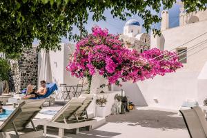 a woman sitting in a chair next to a pool with pink flowers at Villa LuxL in Fira