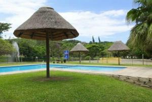 a large umbrella in the grass next to a swimming pool at Peacock Cottage, 95 Eden Wilds in Port Edward