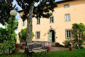 um banco em frente a uma casa com uma árvore em Villa Gherardi - B&B e Hostel em Barga