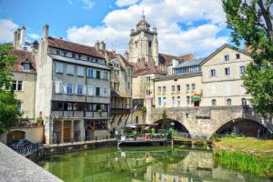 a river in a city with buildings and a boat at La Darbella - Style chalet de montagne in Dole