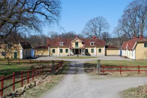 ein Bauernhaus mit einem Zaun und einer Feldstraße in der Unterkunft Gåvetorps Gård in Alvesta