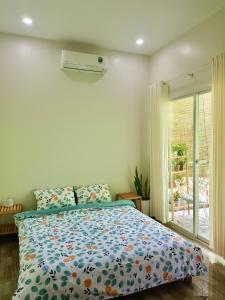 a bedroom with a bed with a floral comforter and a window at Nhiên Homestay - The Green House in Phú Quốc