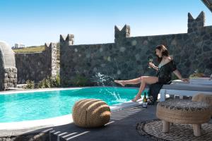 a woman sitting on a table next to a swimming pool at Elements of Caldera Suites in Akrotiri