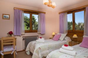 two beds in a bedroom with purple curtains and windows at Hosteria Katy in San Carlos de Bariloche