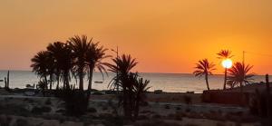 a sunset on a beach with palm trees and the ocean at Dar Chick Yahia Ile De Djerba in Mezrane