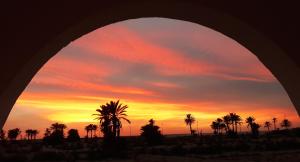 a sunset through an arch with palm trees in the foreground at Dar Chick Yahia Ile De Djerba in Mezrane
