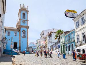 un grupo de personas caminando por una calle con una torre del reloj en Pousada Cor e Arte - Pelourinho, en Salvador