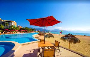 stolik z czerwonym parasolem przy plaży w obiekcie Grand Venetian Beachfront Condos w mieście Puerto Vallarta