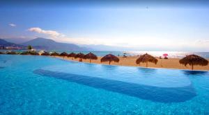 einen Pool neben einem Strand mit Sonnenschirmen in der Unterkunft Grand Venetian Beachfront Condos in Puerto Vallarta