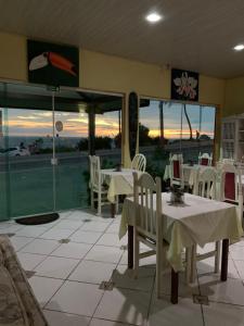 a restaurant with white tables and chairs and windows at Pousada Casa de Pedra in Boicucanga
