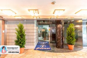 un vestíbulo con dos macetas de árboles frente a un edificio en Tabist Hotel Please Kobe, en Kobe