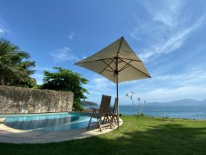 a umbrella and two chairs next to a swimming pool at Casa na praia in Mangaratiba