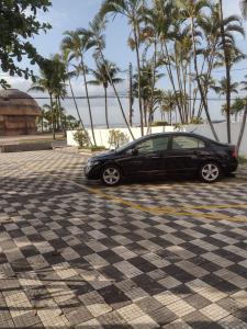a black car parked in a parking lot with palm trees at mar e sol in Praia Grande