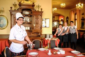 Een man met een koksmuts die eten klaarmaakt in een restaurant. bij Hotel U Bílého koně in Loket