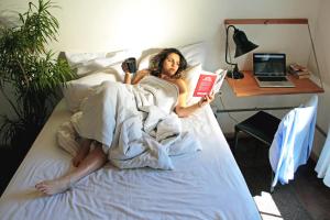 a woman laying on a bed reading a book at CURIOCITY Backpackers Johannesburg in Johannesburg