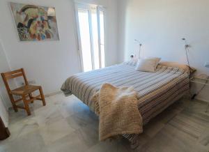 ein Schlafzimmer mit einem Bett mit einem Stuhl und einem Fenster in der Unterkunft Terraza Trafalgar Apartamento tipo penthouse con enorme terraza y vistas al mar in Conil de la Frontera