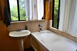 ein Badezimmer mit einem Waschbecken und einer Badewanne neben einem Fenster in der Unterkunft Sanpopo Tree Top Cottage - A Gold Standard Tourism Approved Vacation Home in San Ignacio