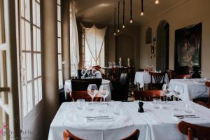 un restaurante con mesas y sillas blancas y ventanas en Hôtel particulier des Jasmins en Le Bar-sur-Loup