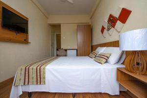 a bedroom with a white bed and a flat screen tv at Imperador Hotel in Poços de Caldas