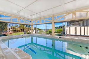 una gran piscina con 2 sillas blancas y una gran pared de cristal en Dunes - Elegant Beach Villa with huge heated swim spa, en Port Fairy