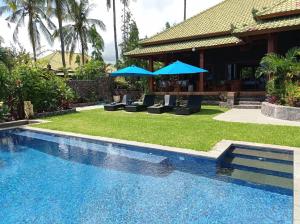 a pool with chairs and umbrellas next to a house at Absolute Beachfront, No neighbours, 3BR Villa with Private Pool on 1200m2 of Tropical Land in Tulamben