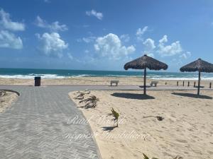 two umbrellas and benches on a beach with the ocean at Beach Way Residence in Aquiraz