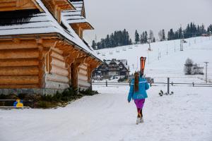 a woman walking in the snow next to a cabin at Sun&Ski Maciejówka Domki Białka Tatrzańska in Białka Tatrzańska