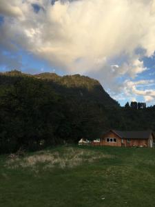 a house in a field next to a mountain at Cabañas Río del Este SPA in Ralún