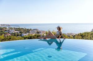 une femme dans un chapeau assise au bord d'une piscine dans l'établissement Villa dei Lecci - 7 Luxury villas with private pool or jacuzzi, à Ischia