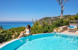 a woman is sitting next to a swimming pool at Villa dei Lecci - 7 Luxury villas with private pool or jacuzzi in Ischia