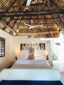a woman sitting on a bed in a room with a ceiling at Paredon Surf House in El Paredón Buena Vista