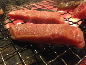 two pieces of meat are cooking on a grill at Minshuku Asogen in Aso