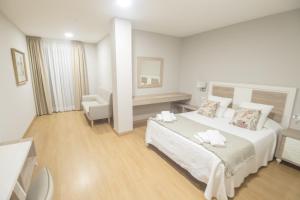a white bedroom with a large bed and a chair at Hotel Roquiño in Caldas de Reis