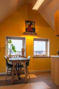 a dining room with yellow walls and a table and two windows at Studio aan Zee in Westkapelle