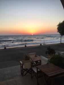 einen Sonnenuntergang am Strand mit einem Tisch und Stühlen in der Unterkunft Anesis Hotel in Agia Pelagia, Insel Kythira