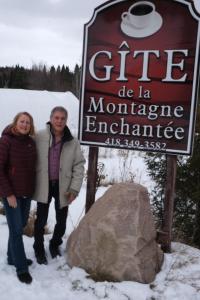 Un uomo e una donna in piedi davanti a un cartello di Gîte de la Montagne Enchantée a Metabetchouan