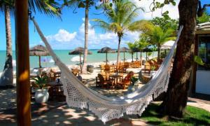 a hammock on a beach with chairs and tables at Residencial Mont Sião II - Tonziro in Porto Seguro